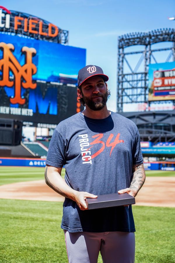 MLBPA - MLB player holding gift box with Mets logo behind